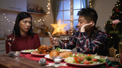 Asian man addictive to phone is ignoring his girlfriend who’s staring at him and cutting food in...