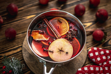 Pot with fragrant spicy hot mulled wine on a wooden table surrounded by festive accessories and...