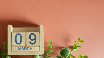 March 9, Date design with calendar cube and leaf on orange background.