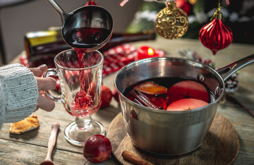 Woman is pouring fragrant hot spicy mulled wine into a clear glass. Concept of a cozy festive atmosphere, New Year and Christmas mood