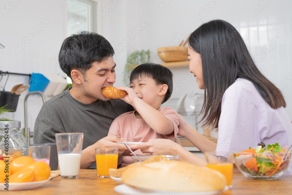 Wall mural Happy refreshment family breakfast in morning, asian young parent father, mother and little cute boy, child having meal in kitchen eating together at home. Cheerful, enjoy cooking people.