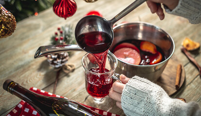 Woman is pouring fragrant hot mulled wine into a clear glass. Concept of a cozy festive atmosphere,...