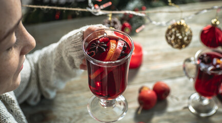 Woman in a sweater is drinking fragrant hot mulled wine, decorated with fruits and spices and enjoying a pleasant evening. Concept of a cozy festive atmosphere, New Year and Christmas mood