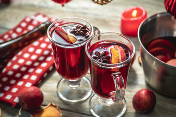 Spicy aromatic hot mulled wine in a saucepan and a clear glasses on a wooden table with festive accessories. Concept of a cozy holiday atmosphere, New Year and Christmas mood