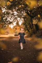 Adorable little toddler girl walking down autumn path with hands in pockets and fall foliage