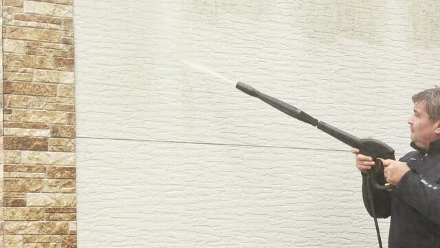 Man cleaning walls with high pressure power washer. Washing cladding walls house.
