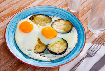 Plate with appetizing fried eggs, cooked with sliced and roasted eggplant