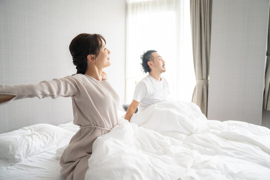 部屋の中で逆光の朝日を浴びてストレッチをする日本人の夫婦1