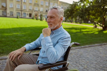 Elderly man in wheelchair riding alone on a walk in the park on a summer day