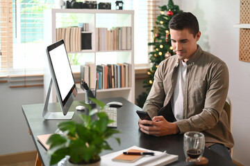 Man sitting in front of computer and using smart phone.