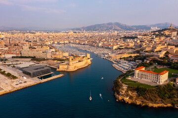 Obraz premium Picturesque drone view of modern Marseille cityscape on Mediterranean coast overlooking large Old Port with moored pleasure yachts and Fort Saint-Jean on sunny day, France