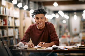 Young happy black student learning in a library and looking at camera.