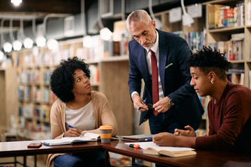 Mature teacher assisting his African American students wo are learning in a library.