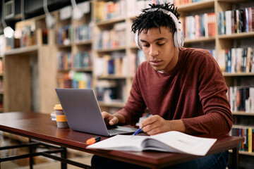 Young African American student using laptop while learning in a library.