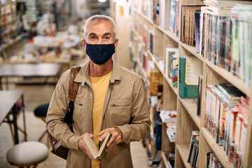 Happy mature man wearing protective face mask while studying in library during coronavirus pandemic.
