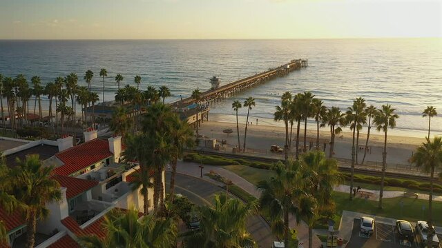Aerial view of the pier in San Clemente, California, over the top of tall palm trees