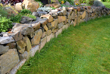 the dry wall serves as a terrace terrace for the garden, where it holds a mass of soil. the wall is slightly curved, which helps it to stabilize better. planting perennials and rock gardens - obrazy, fototapety, plakaty