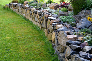 the dry wall serves as a terrace terrace for the garden, where it holds a mass of soil. the wall is slightly curved, which helps it to stabilize better. planting perennials and rock gardens