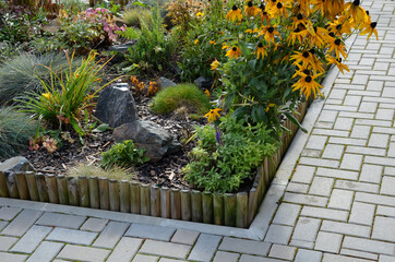 a colorful perennial flowerbed at the entrance to the garden bordered by a decorative wooden palisade. from the back it is connected by a wire. flowers and stones bloom in the autumn sun.