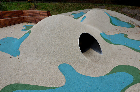 dreamy white rubber landscape with scoops and colorful spots on the playground. stainless steel tunnel through the wave. design corner bench lined with wood part of the retaining wall made of concrete