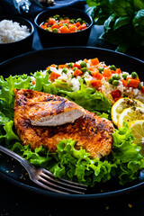 Fried chicken breast with white rice, green peas and carrots on black wooden table