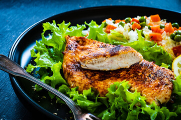 Fried chicken breast with white rice, green peas and carrots on black wooden table