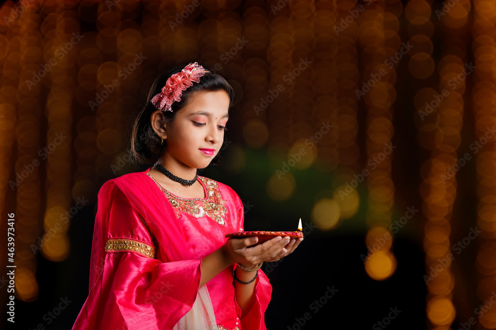 Wall mural Cute Indian little girl holding diya or oil lamps for Diwali Celebration.