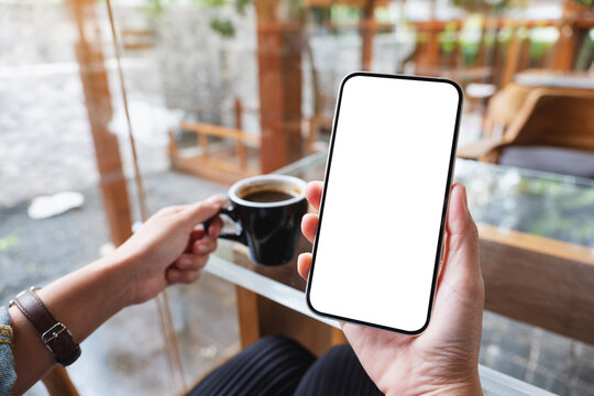 Mockup image of hands holding mobile phone with blank desktop screen while drinking coffee