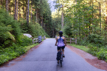 Fototapeta premium Adventurous White Caucasian Woman on a bicycle riding on a path in Green Canadian Rain Forest. Seymour Valley Trailway in North Vancouver, British Columbia, Canada.