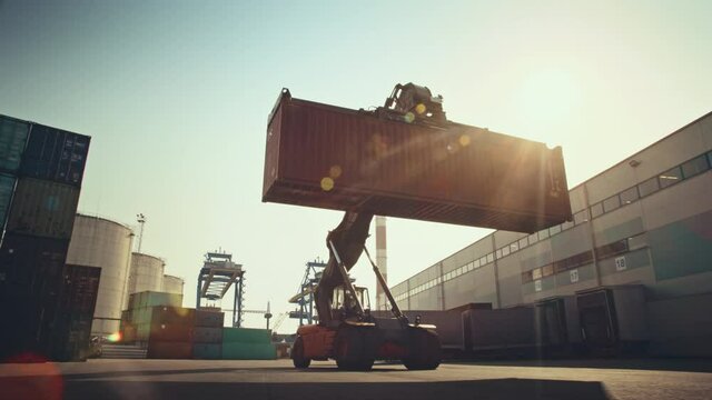 Industrial Scene with Computer Generated Double Girder Gantry Cranes Working in the Background of a Container Handler Carrying a Large Shipping Container in a Shipyard Logistics Center Terminal.