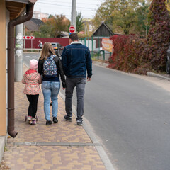 Obraz premium Dad, mom and daughter walk on the pedestrian sidewalk next to the car road on a cloudy autumn day