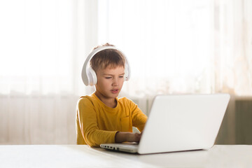child boy in headphones is using a laptop and study online with video call teacher at home. homeschooling, distant learning 