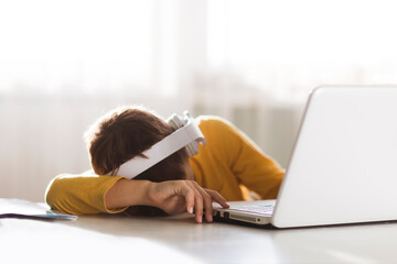 tired schoolboy sleeps with his head on a table in front of a laptop. homeschooling, distant...
