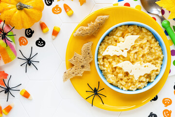 Fun Food for kids - Halloween pumpkin risotto with cinnamon decorated with bat shaped pieces of cheese and festive decorations like spiders, corn candies and pumpkins