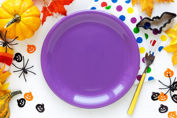 Halloween table setting for kids. Bright purple plate with festive decorations, pumpkins and spiders
