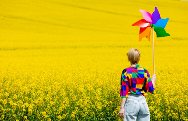 Beautiful female in 90s stylish shirt with pinwheel in rapeseed field