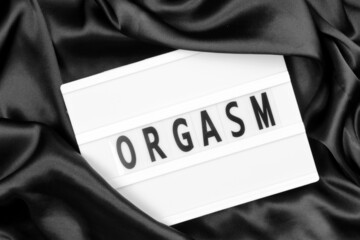 Photo of a light box with text orgasm on black fabric background