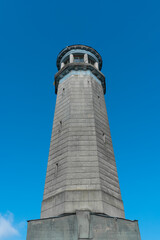Fototapeta na wymiar The old stone building of the lighthouse rises against the blue sky, vertical photo