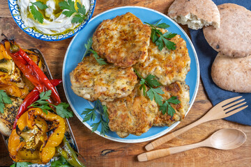 Chicken shawarma latkes, grilled vegetables, hummus plate, pita bread on blue wooden background.