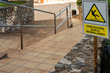 Close-up of the slippery ground caution sign, written in Spanish language. In the background, an...