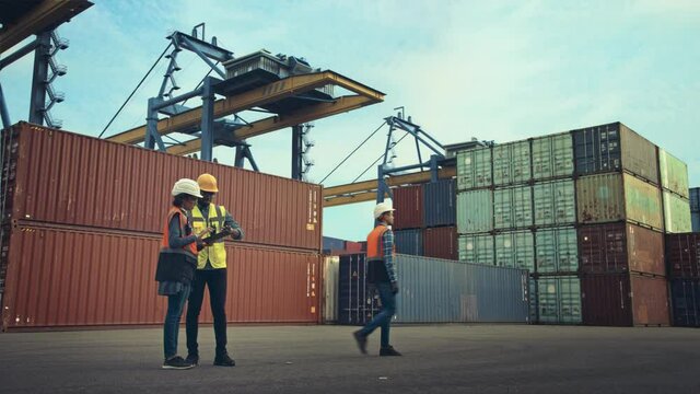 Multiethnic Female Industrial Engineer with Tablet and Black African American Male Supervisor in Hard Hats Stand in Container Terminal. VFX Double Girder Gantry Cranes Work in the Background.
