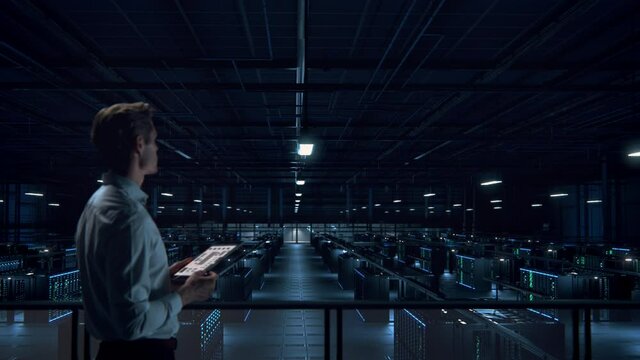 IT Specialist Uses Tablet Computer in Data Center Room. Server Farm Cloud Computing Facility with Maintenance Administrator Working. Cyber Security Engineer Working in Personal Network Protection.