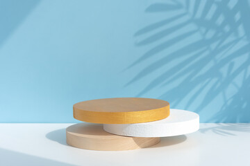 Wooden, white and gold scenes on a white table on a pastel blue background with a shadow of palm leaves. Premium podium for advertising your product. Background for the product presentation.