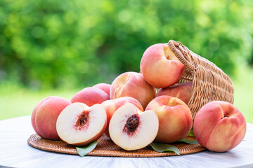 Fresh peach with slices on blurred greenery background, Peach fruit in Bamboo basket on wooden table in garden
