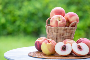 Fresh peach with slices on blurred greenery background, Peach fruit in Bamboo basket on wooden table in garden