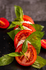 Caprese salad made of fresh juicy red tomatoes, white mozarella, fresh basil leaves and virgin olive oil on a black board. Selective focus.