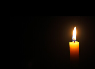 Close up single yellow candle light and flame on black background
