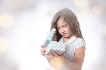 Beautiful girl with curls with a gift in her hands and a mysterious look on a festive background with bokeh, portrait.
