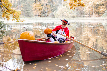 young man dressed as gondolier in gondola boat decorated with pumpkins on pond in autumn park celebrates Halloween and having fun, concept of Halloween carnival or costume party © klavdiyav