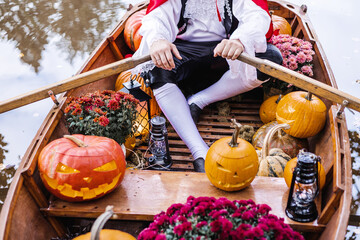 young man dressed as gondolier in gondola boat decorated with pumpkins on pond in autumn park celebrates Halloween and having fun, concept of Halloween carnival or costume party © klavdiyav